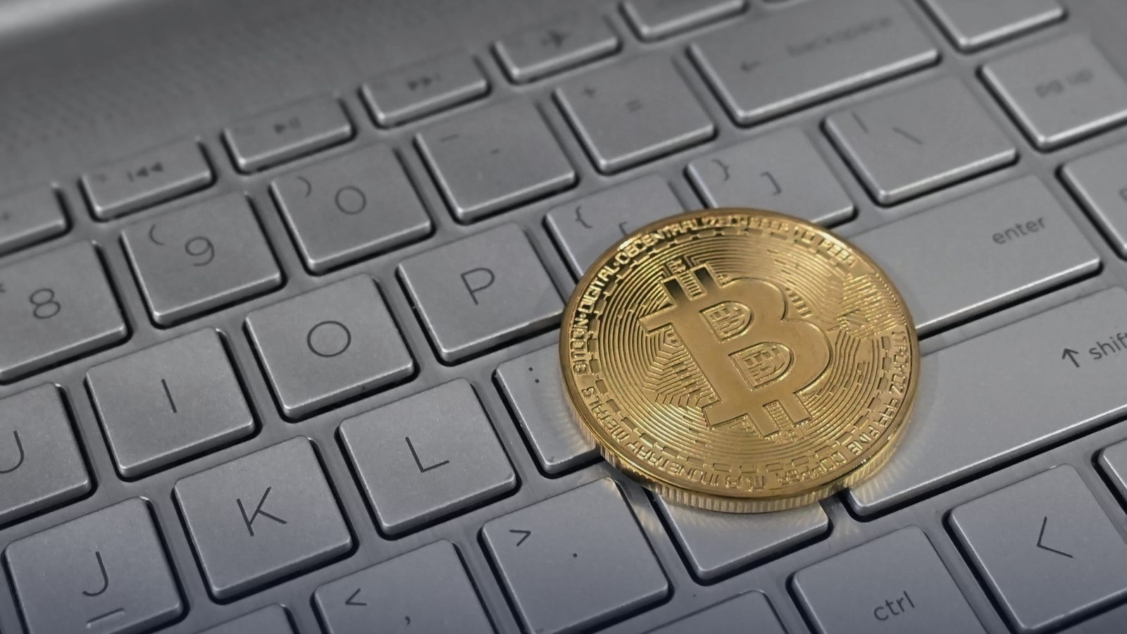 A gold bitcoin token resting on a laptop keyboard