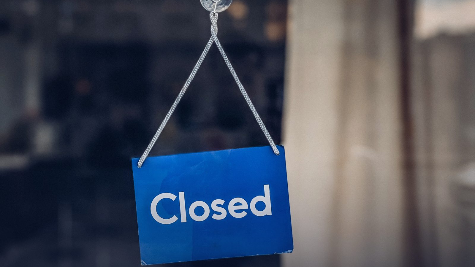 A blue “Closed” sign hanging on a glass shop door