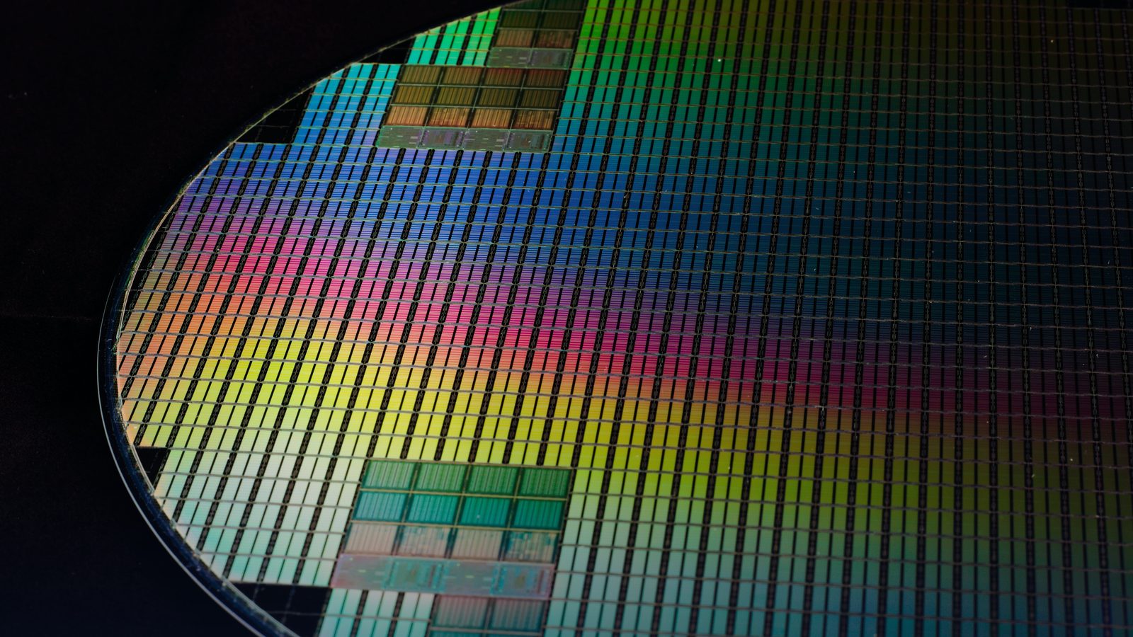 A silicon wafer patterned with rows of chips, catching coloured light