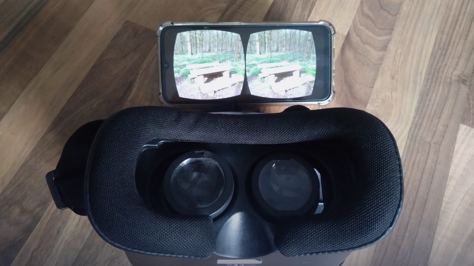 A virtual reality headset and a smartphone showing a stereoscopic image, on a wooden table